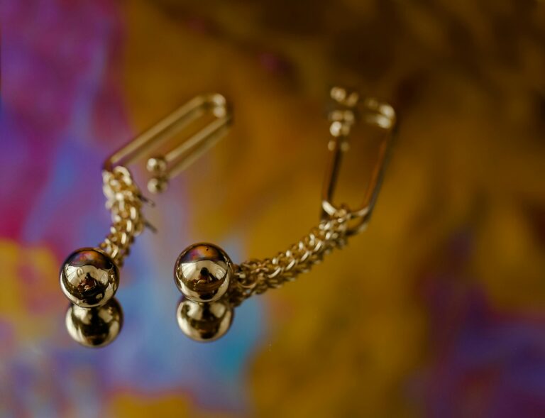 Close-up of luxury gold earrings with a detailed chain on a colorful background.