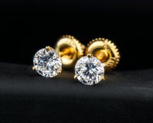 Close-up of luxurious gold and diamond stud earrings on a black surface.